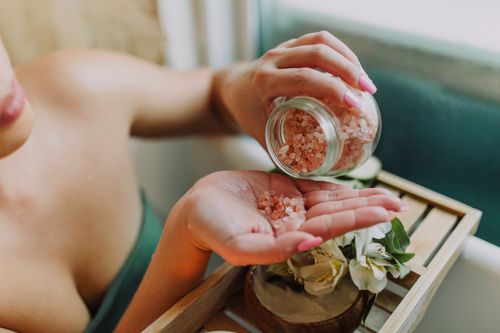 Free Close-up of hands pouring pink bath salt with flowers in a relaxing spa setting. Stock Photo