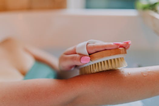 Close-up of a hand using a dry brush on an arm in a relaxing bath setting.