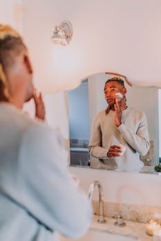 A man applying face cream while looking in the bathroom mirror, focusing on skincare routine.