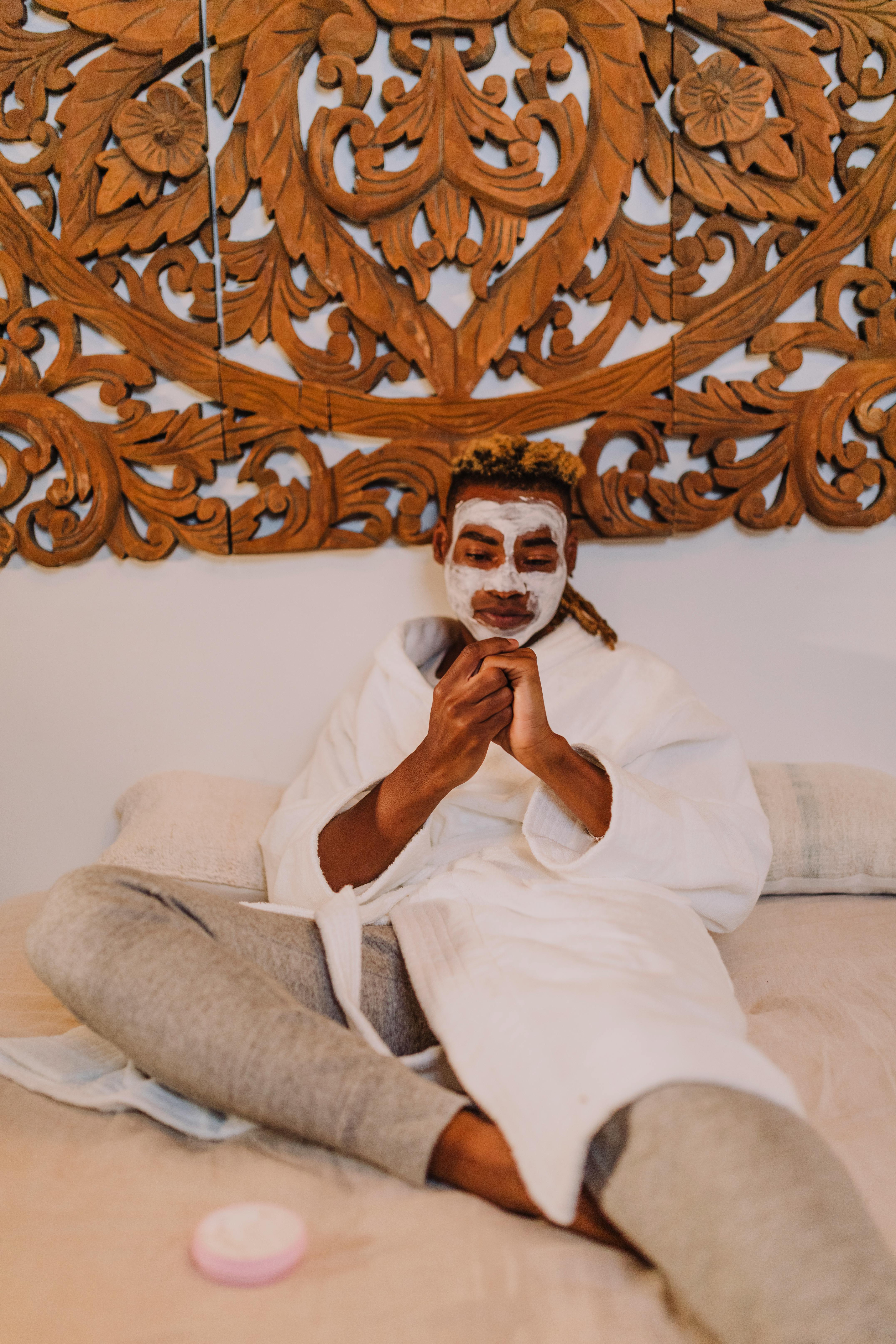 A Person Wearing White Robe with Cream on Face Sitting on Bed Rubbing his  Hands · Free Stock Photo