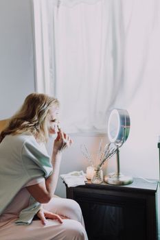 Woman enjoying a peaceful skincare ritual beside a bright window.