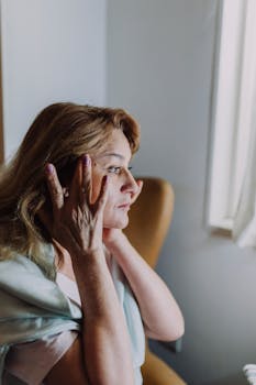 A woman gently applying skincare, embracing self-care in a serene indoor setting.