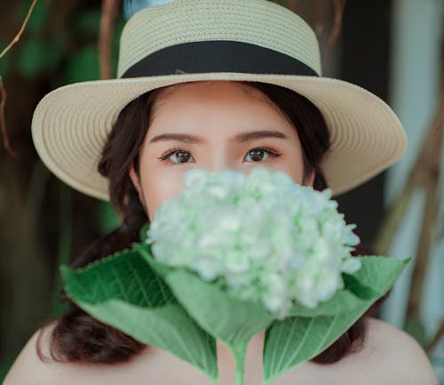 Wanita Mengenakan Topi Putih Memegang Bunga