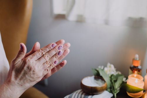 Free Hands applying skincare product in a cozy, natural setting with candles, creating a relaxing atmosphere. Stock Photo