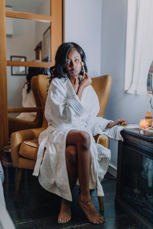 A Woman in White Bathrobe Massaging her face with a Jade Roller
