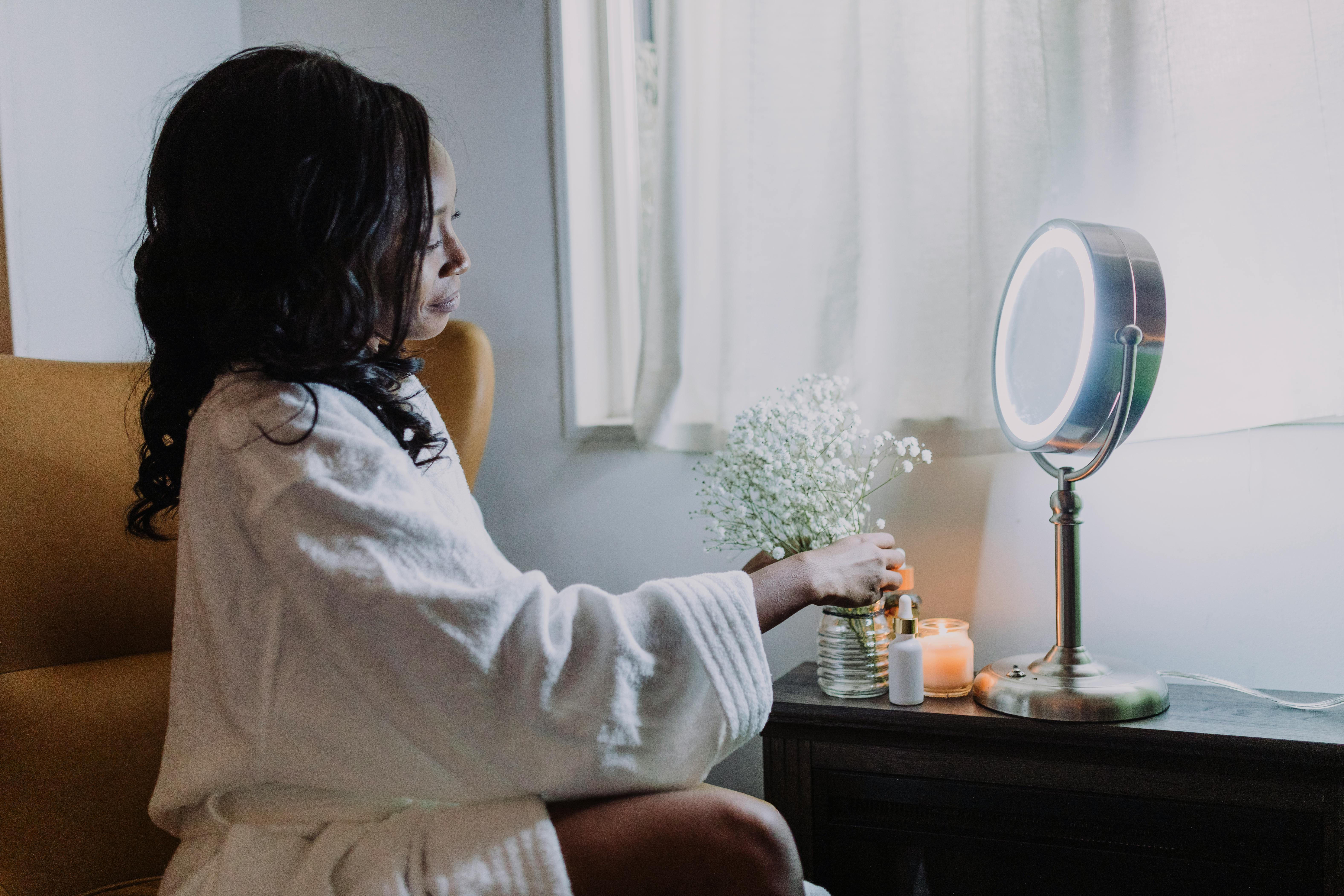 Free A woman arranges baby's breath flowers by a lit mirror in a warm indoor setting. Stock Photo