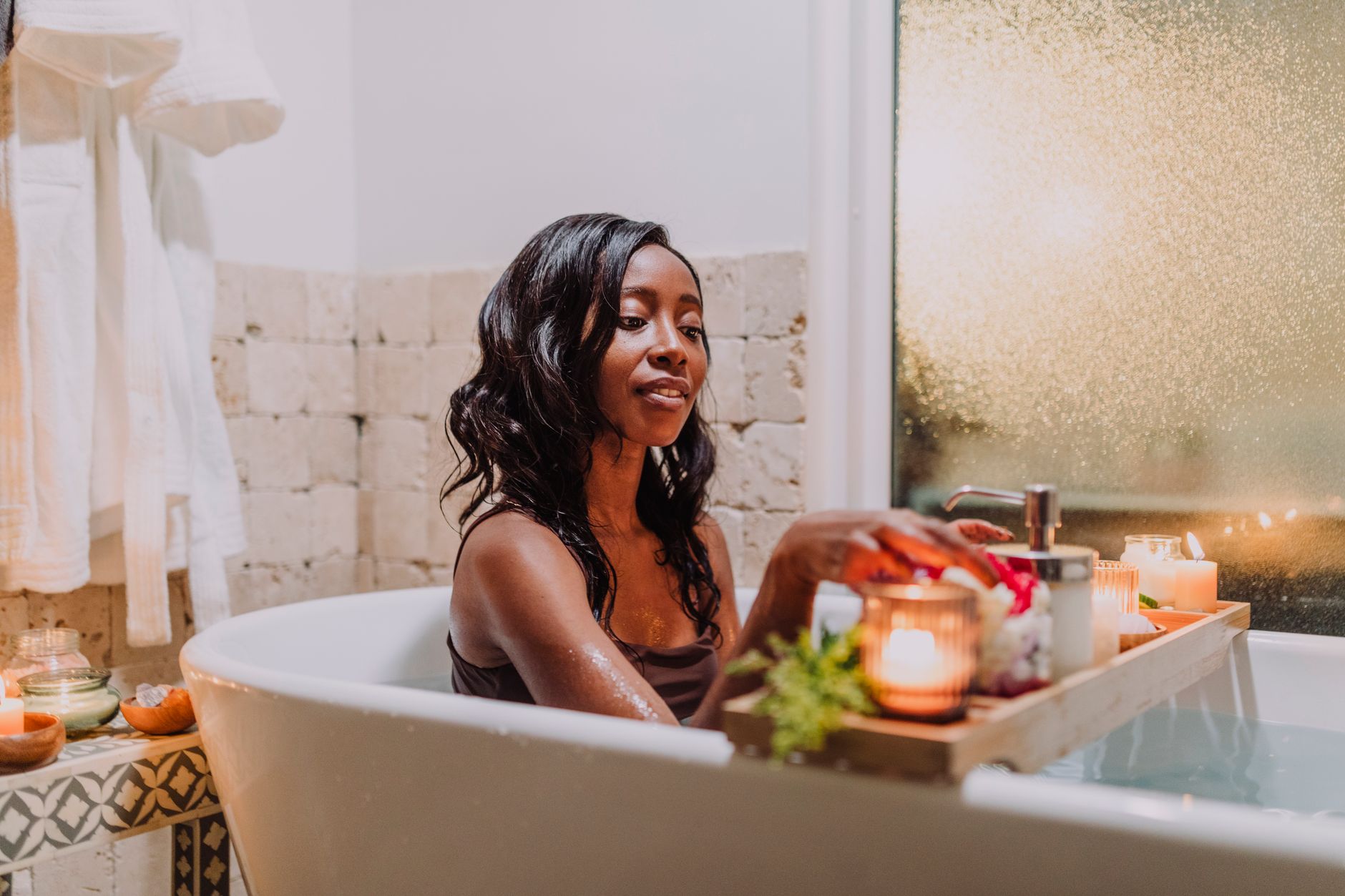 Woman relaxing in a cozy bath with candles and a tray for a calming spa experience.