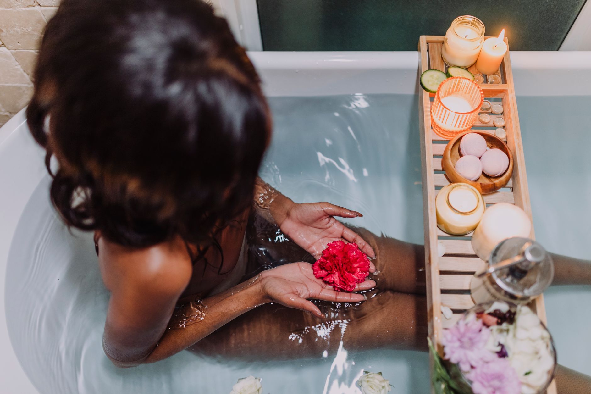 A woman enjoying a spa-like bath with floating candles and flowers, creating a peaceful atmosphere.