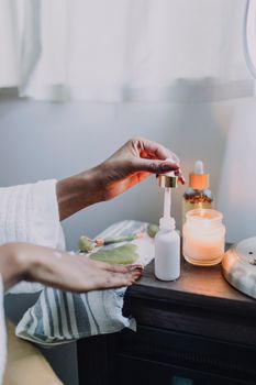 Hand using a dropper bottle in a calming skincare setup with candles.