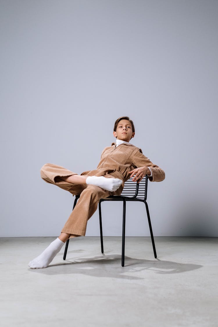 A Boy In Brown Long Sleeves And Pants Sitting On The Chair