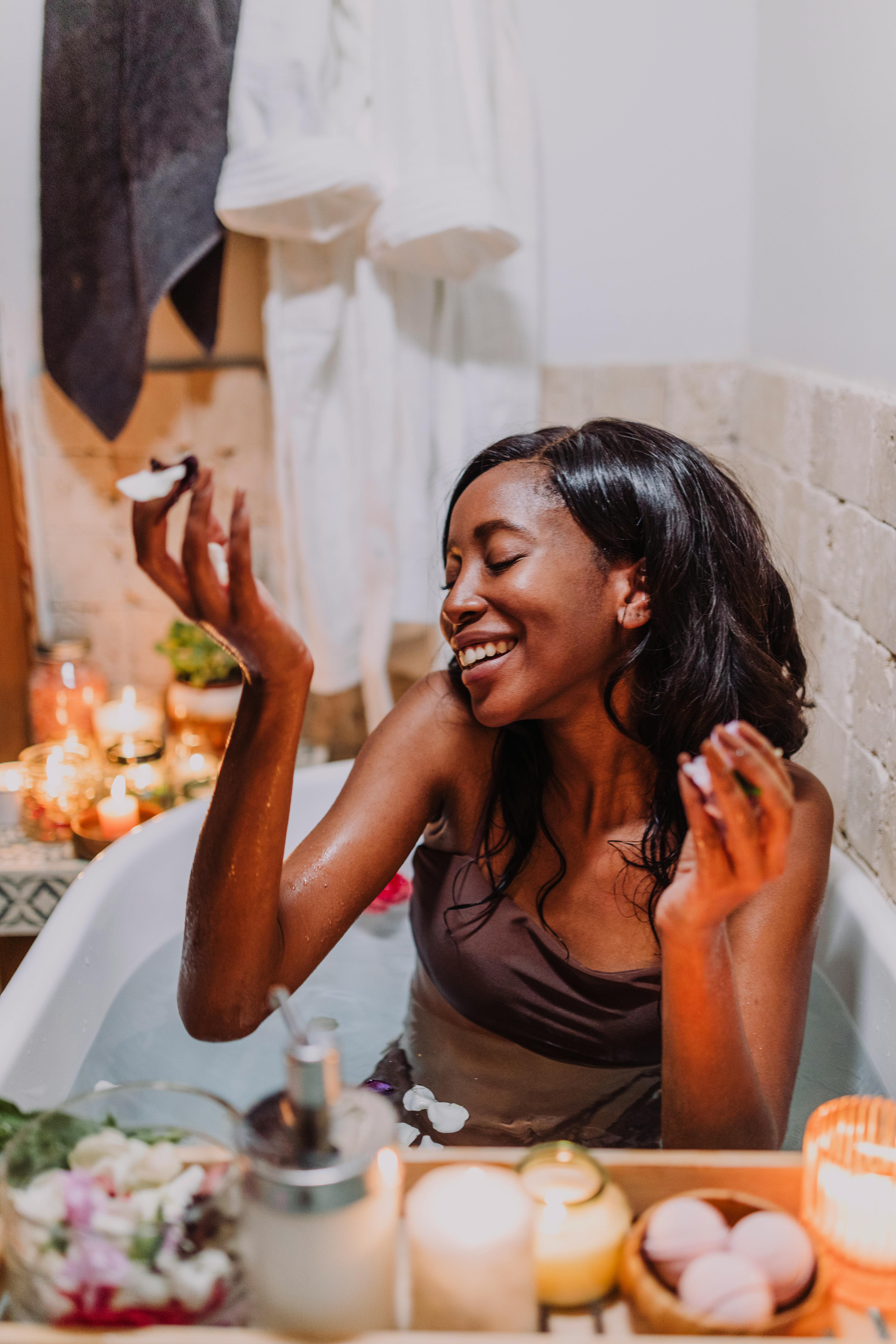 A joyful woman enjoying a relaxing bath with flower petals, candles, and bath essentials.