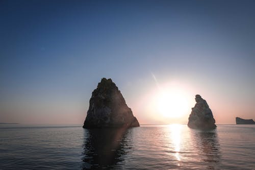 Spectacular scenery of sharp rocky cliffs in rippling water of endless ocean against amazing cloudless sunset sky