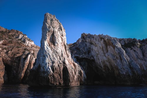 Picturesque rocky cliffs with grotto washing by rippling sea water against bright cloudless blue sky on sunny day