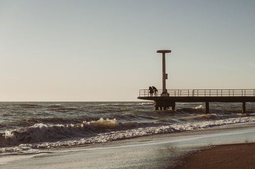 Free A serene seaside scene featuring a wooden pier extending into the ocean under a tranquil sunset sky. Stock Photo
