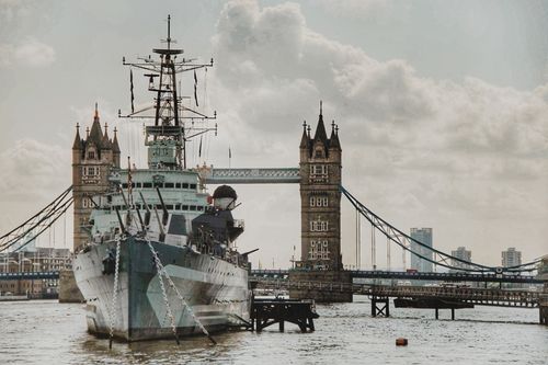 Free View of a historic warship sailing near London's iconic Tower Bridge on the River Thames. Stock Photo