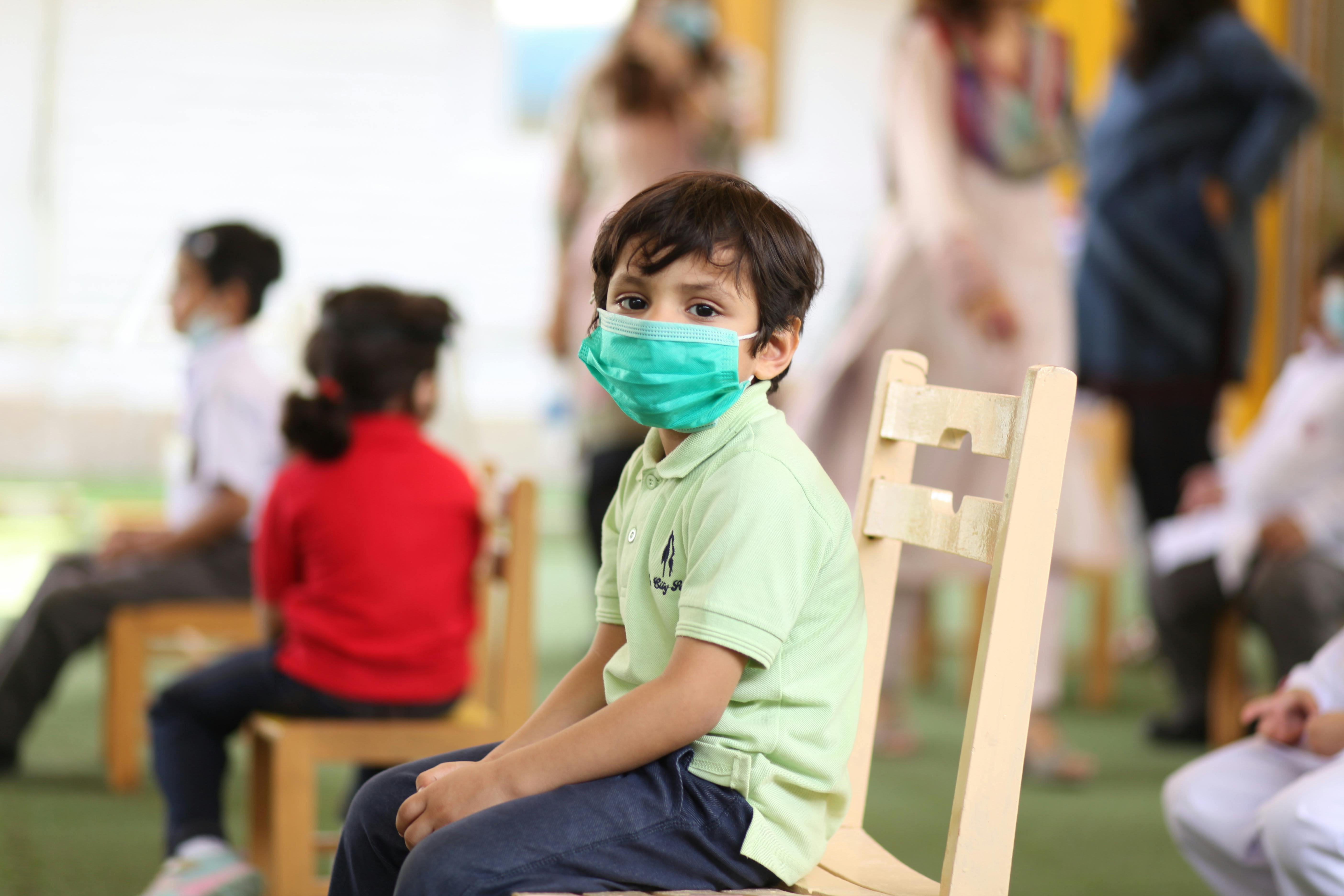 children in face masks sitting on chairs and waiting