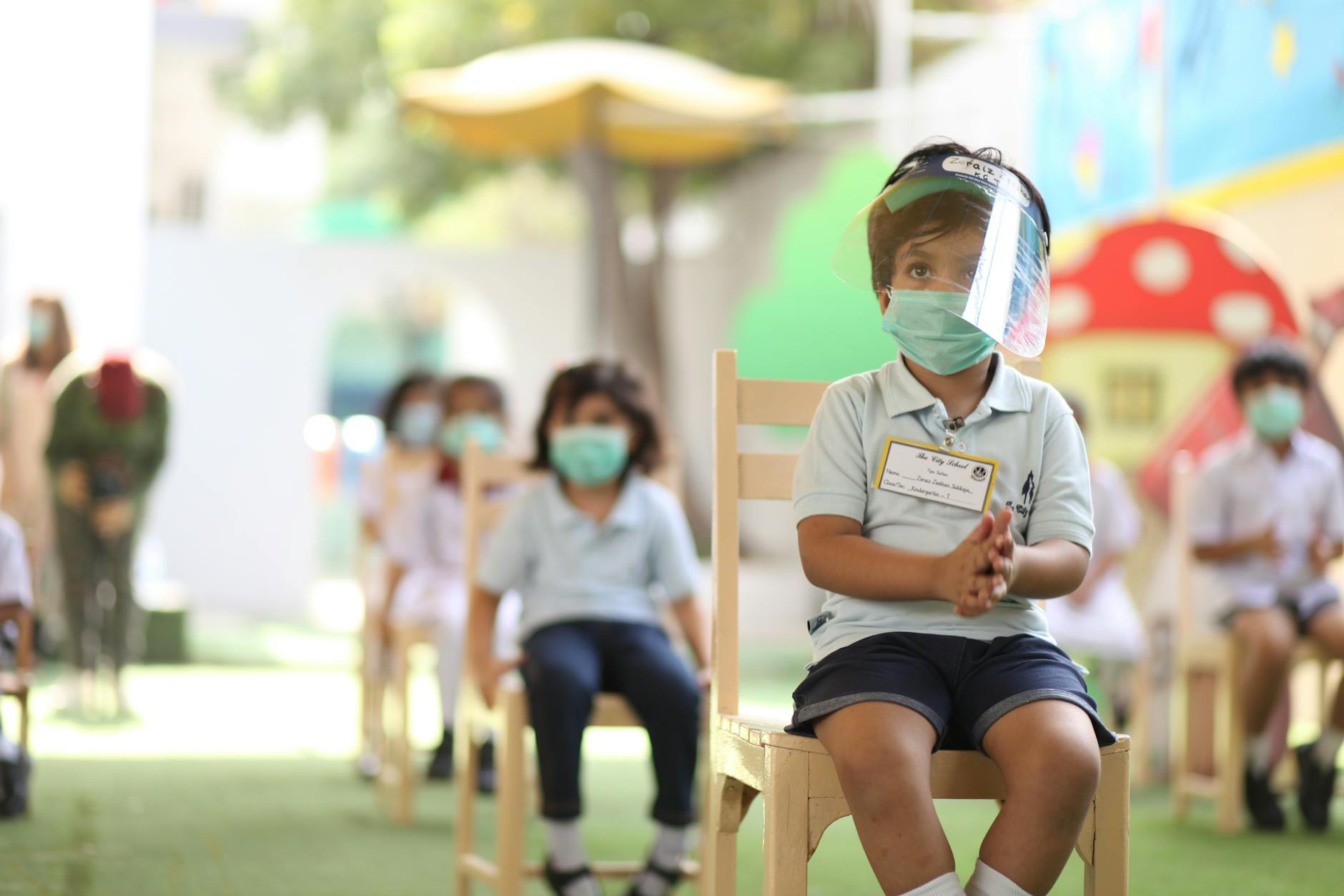Children sitting in a classroom wearing face masks and shields for safety.