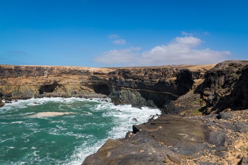 Free A stunning coastline view with rocky cliffs and waves crashing along the seashore under a bright blue sky. Stock Photo