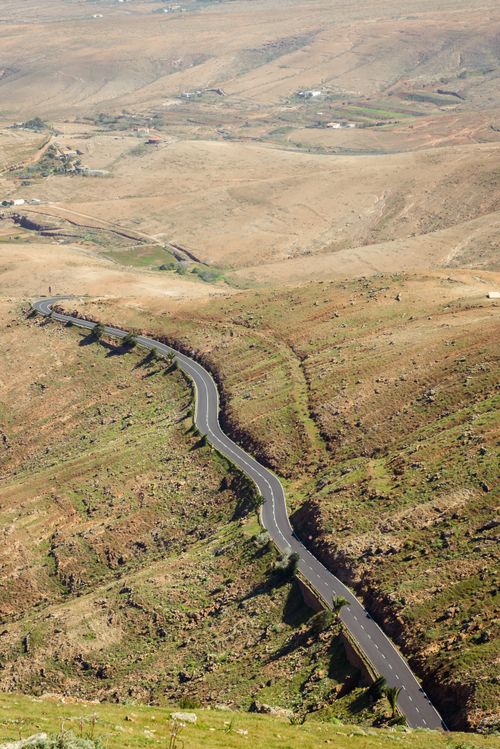 Free Aerial view of a winding road cutting through an arid, rural landscape with sparse vegetation. Stock Photo