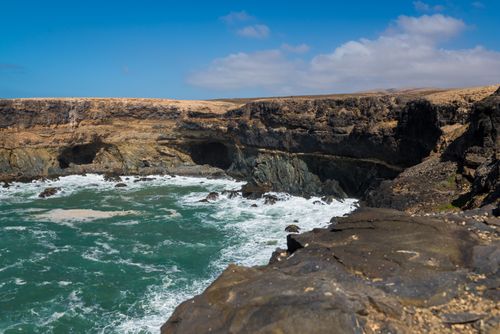 Free Captivating coastal scene with rugged cliffs and crashing waves under a clear sky. Stock Photo