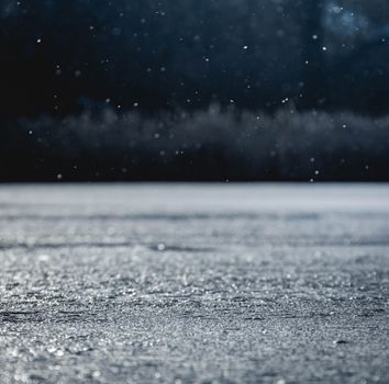 Close-up view of snow falling on a reflective frozen lake during winter, capturing the tranquil atmosphere.