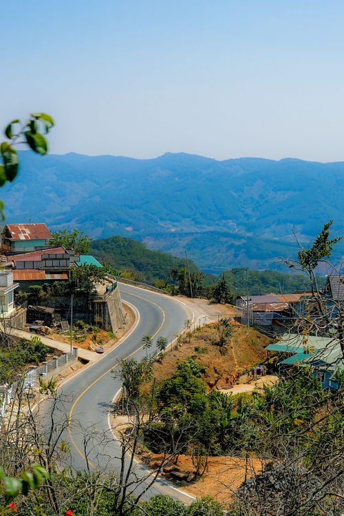 Free A curvy road winds through hillside houses, framed by mountains in the background. Stock Photo
