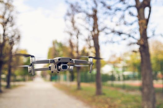 Close-up of a drone hovering along a tree-lined pathway in fall.