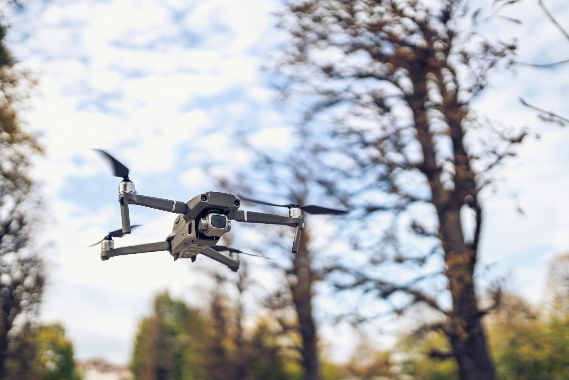 Drone in flight among trees with a clear sky background, showcasing technology and nature.