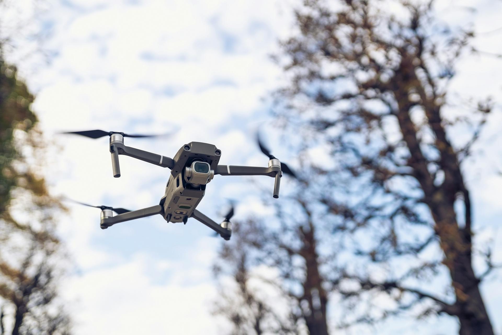 A close-up shot of a drone flying near trees against a clear blue sky, highlighting modern technology.