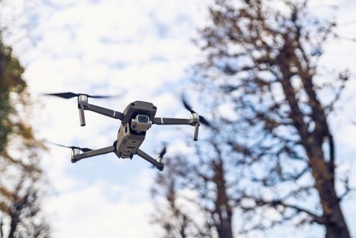 Free A close-up shot of a drone flying near trees against a clear blue sky, highlighting modern technology. Stock Photo