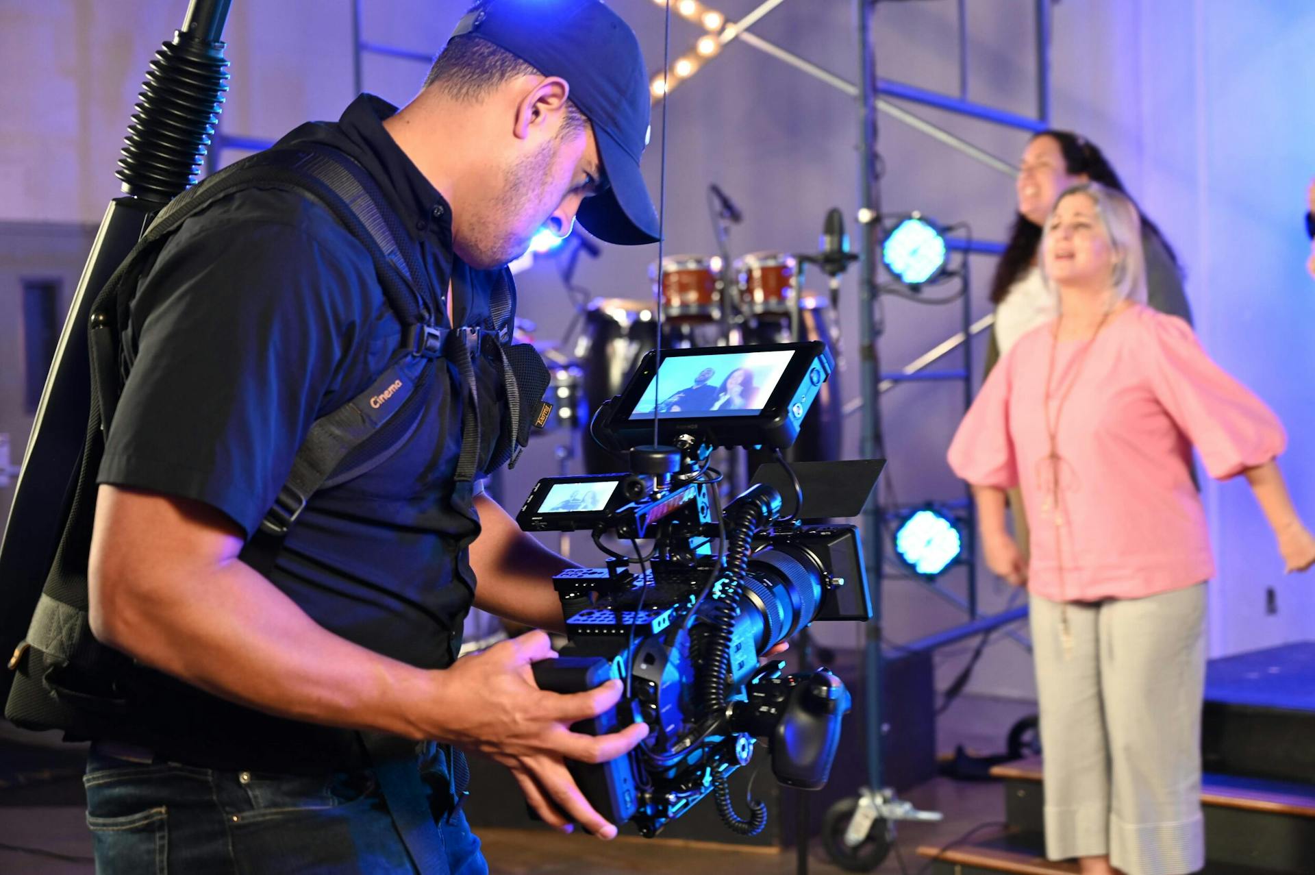 Cameraman capturing live event with professional video equipment inside a vibrant venue.