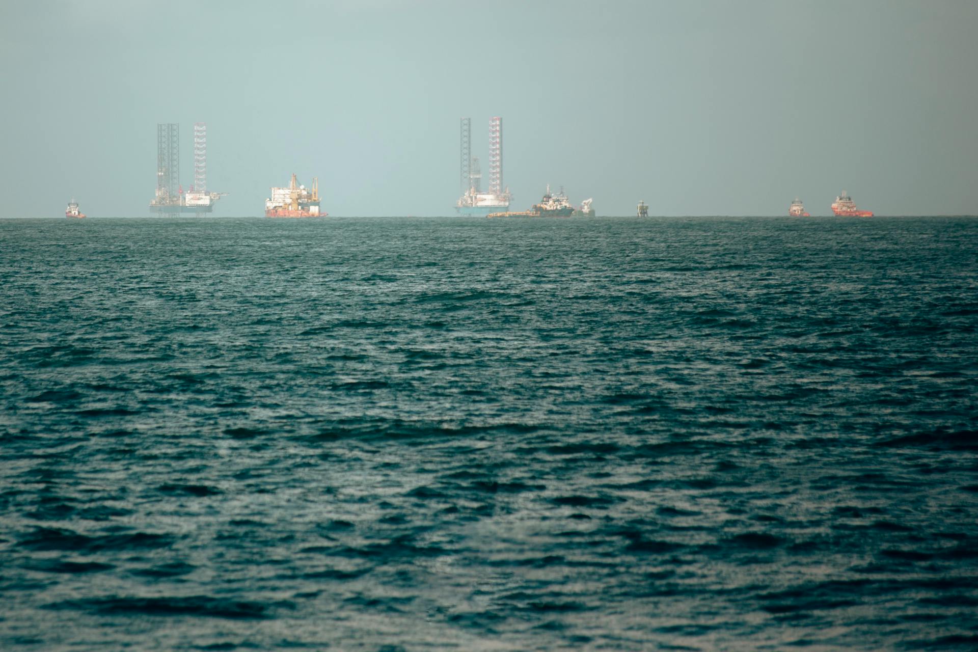 A scenic view of offshore vessels and oil rigs set against a calm ocean horizon, evoking a sense of maritime journey.