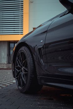 Detailed shot of a black car's wheel against urban architecture, highlighting modern design.