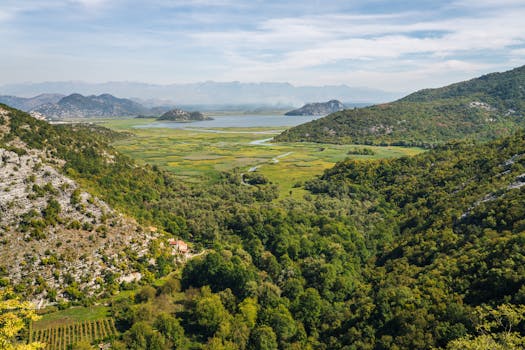A stunning aerial view capturing lush green valleys, a serene lake, and distant mountain ranges under a clear sky.