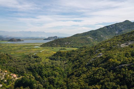 Scenic panoramic view of verdant mountains and a tranquil lake under a blue sky, showcasing nature's beauty.