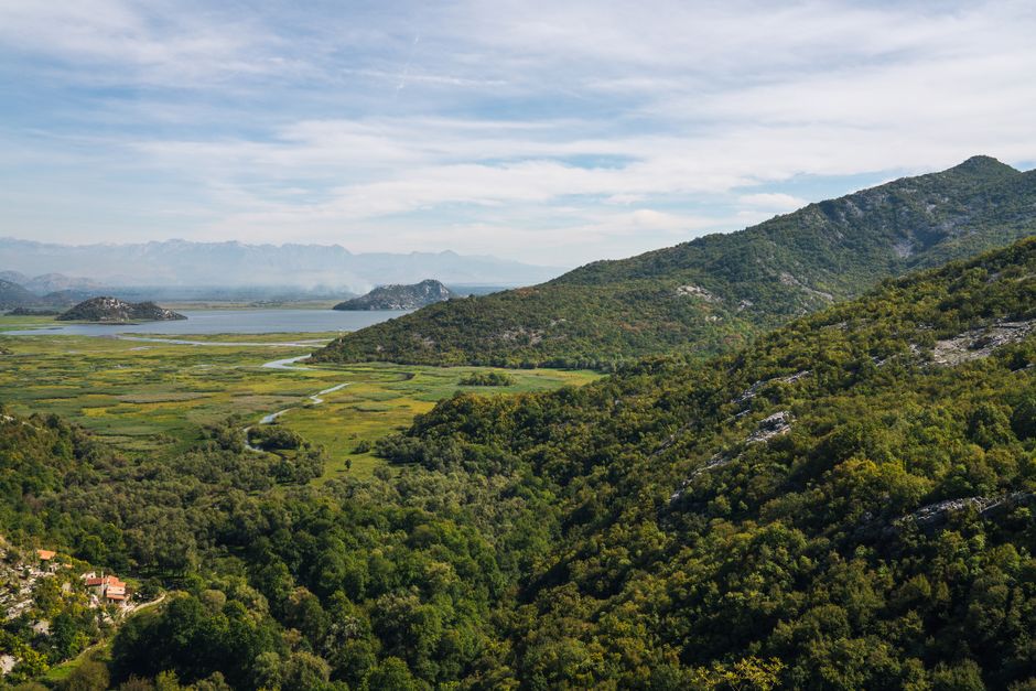 Scenic panoramic view of verdant mountains and a tranquil lake under a blue sky, showcasing nature's beauty.