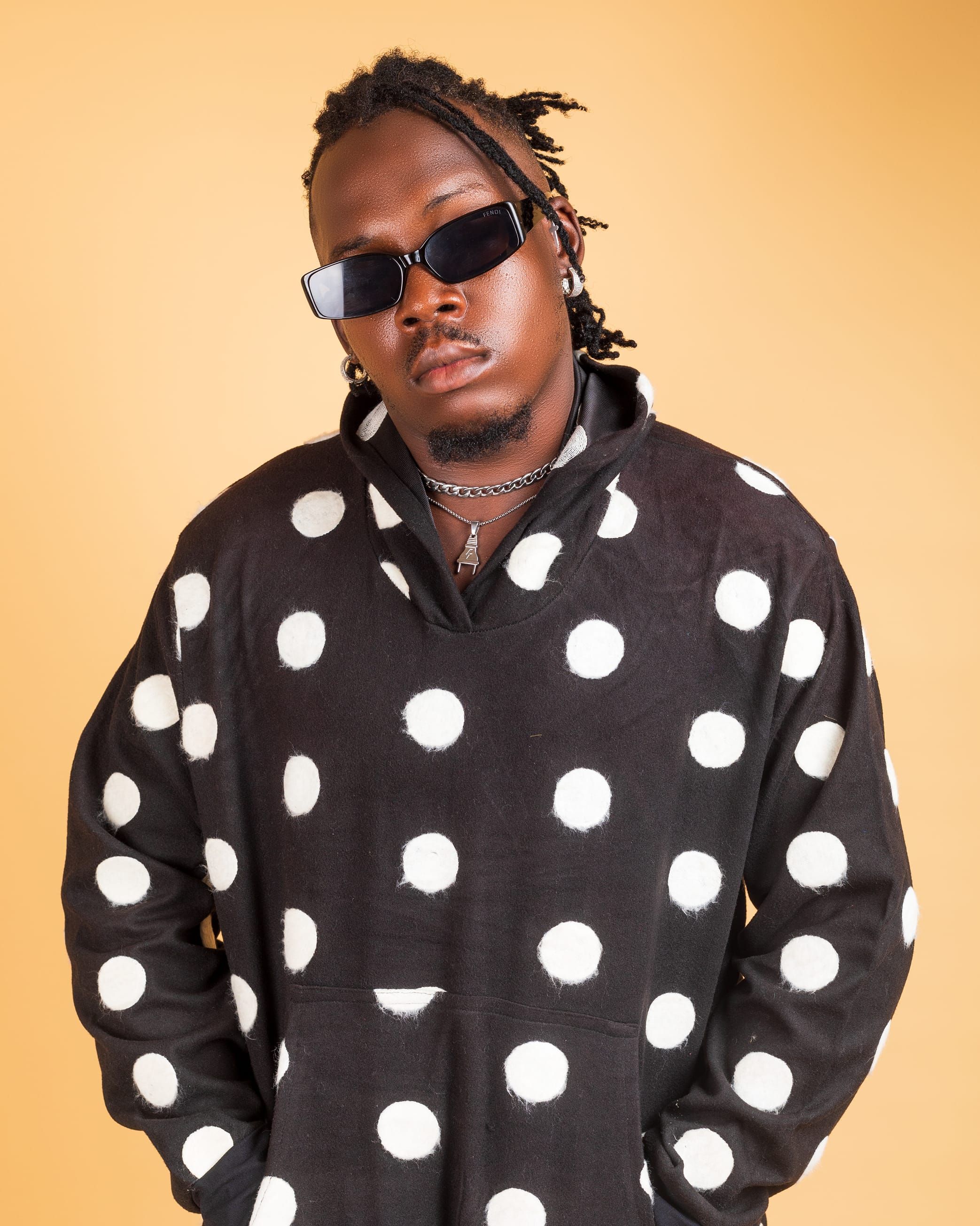 Fashionable portrait of a young man with sunglasses and polka dot sweater on yellow background.
