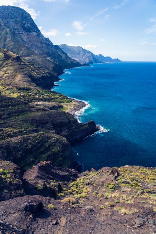 Free Stunning aerial shot of a rugged mountain coastline meeting vibrant blue ocean waters. Stock Photo