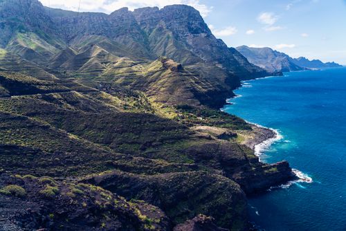 Free A stunning aerial view of dramatic mountains and vibrant blue ocean along a rugged coastline. Stock Photo