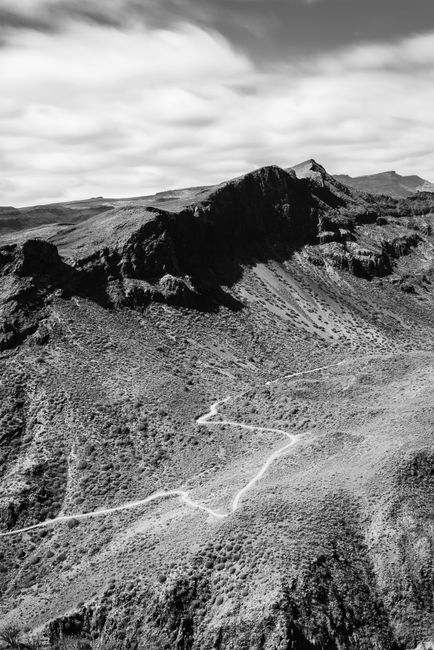 Stunning black and white mountain view with winding trail under cloudy sky.