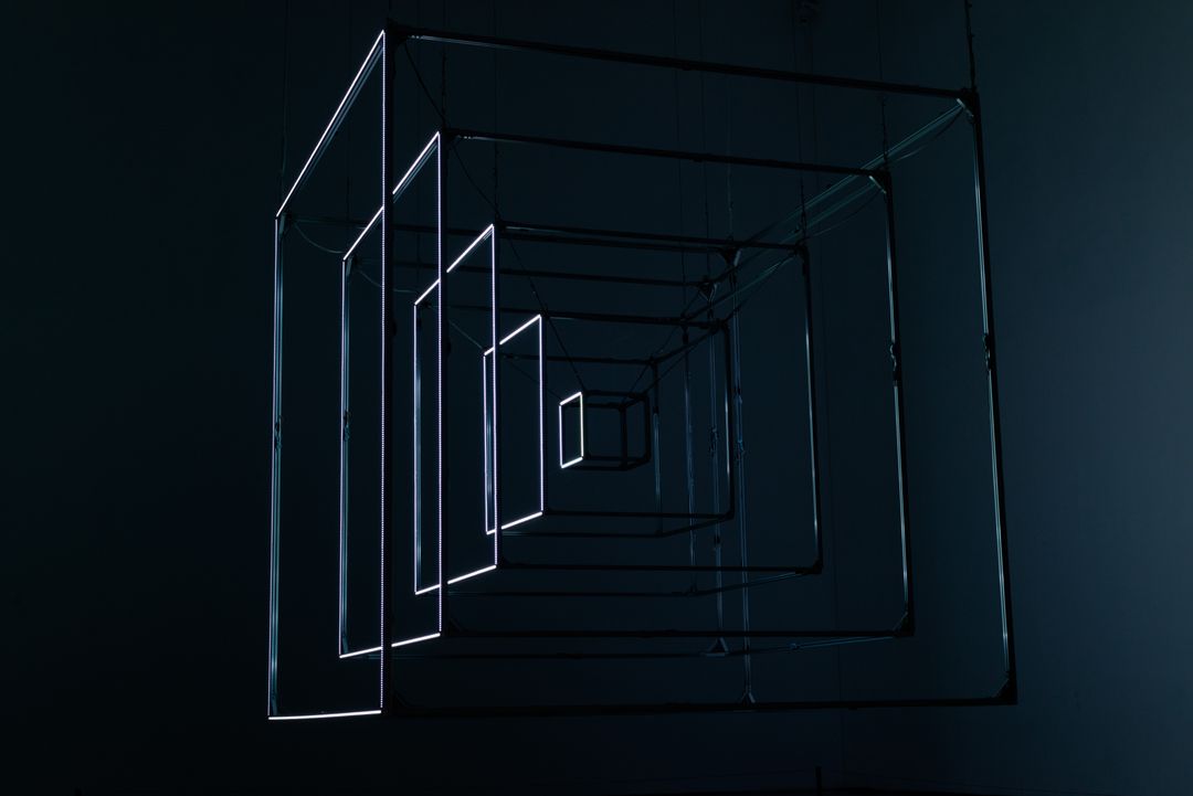 Abstract metal cube installation with glowing edges in a dark room, showcasing geometric art.