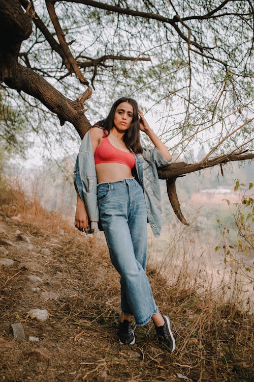 Trendy young woman leaning on tree in forest