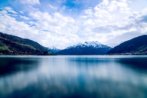 Free Tranquil lake reflecting snow-capped mountains under a vivid blue sky. Stock Photo