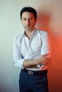 Bearded adult male entrepreneur in white shirt with folded arms looking at camera against wall with shade
