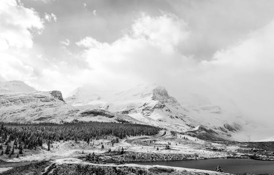 Serene black and white landscape featuring a snow-capped mountain and a lake.