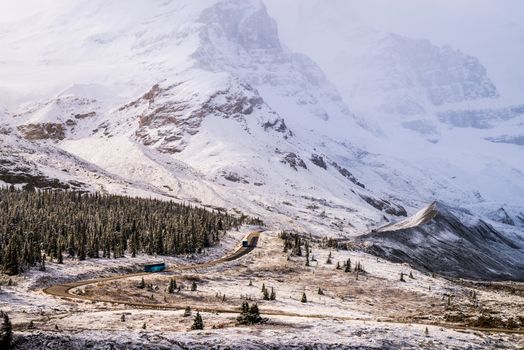 A winding road through snow-covered mountains and evergreen forests under a bright sky.