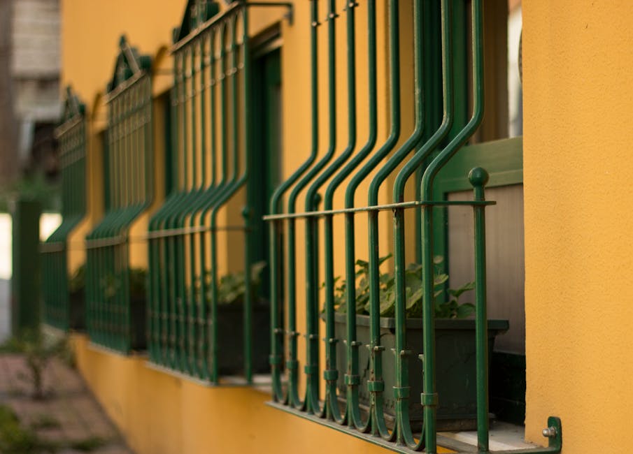 Green iron grills on yellow wall with potted plants in sunny urban setting.