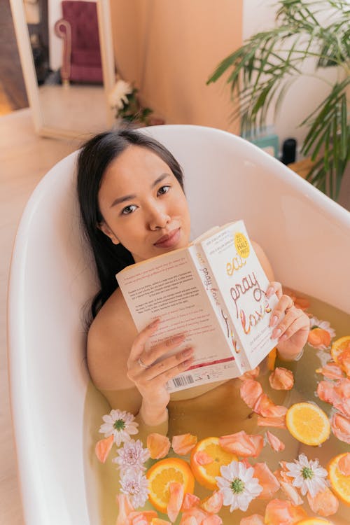 Free Woman Lying in a Bath with Floating Flowers and Reading a Book  Stock Photo