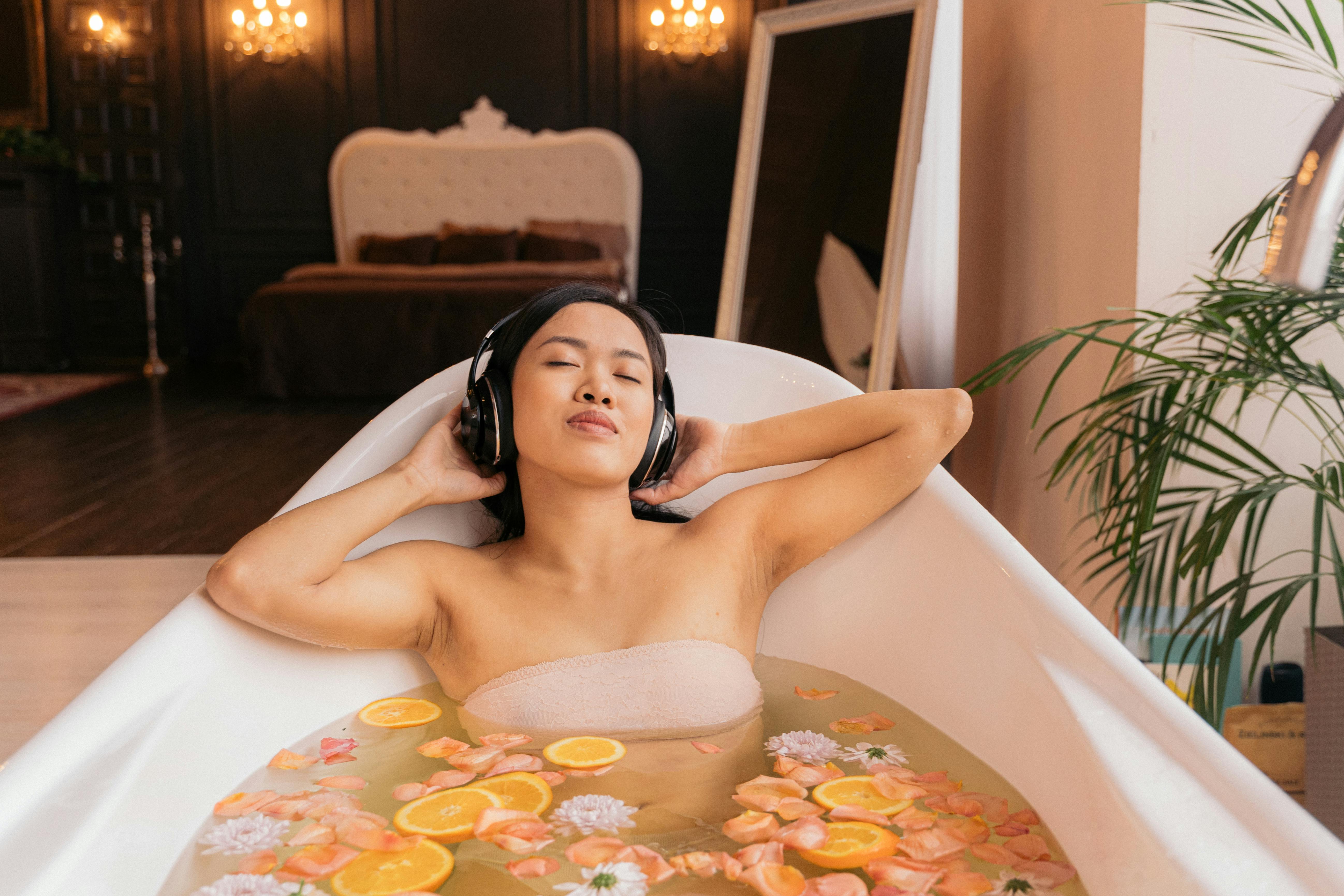 Woman enjoys a soothing floral bath, listening to music with headphones for ultimate relaxation.