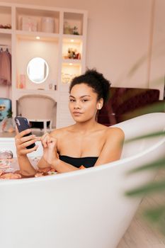 Woman enjoying a relaxing bath while using a cellphone indoors.